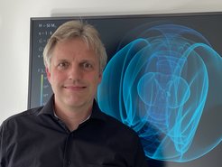 Portrait of Harald Pfeiffer in front of a poster with blue gravitational waves.